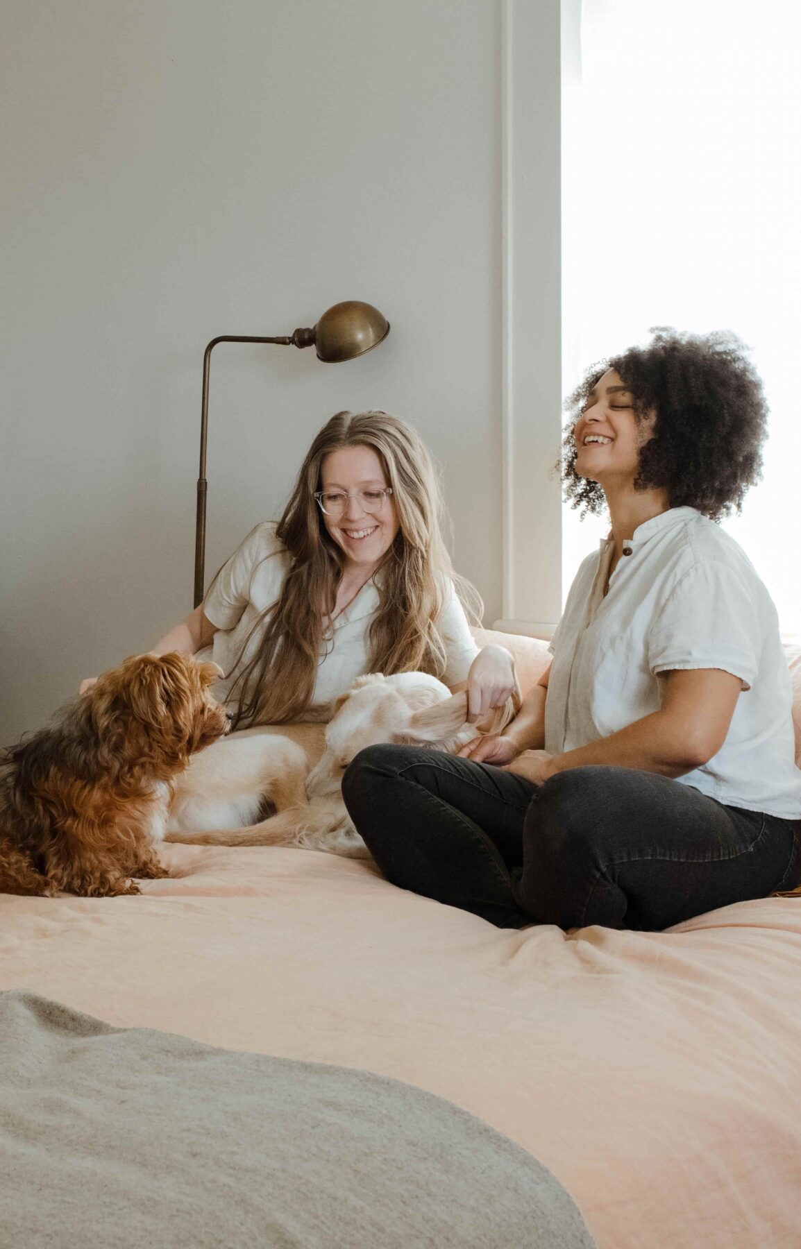 two women sitting on a bed with a dog laughing